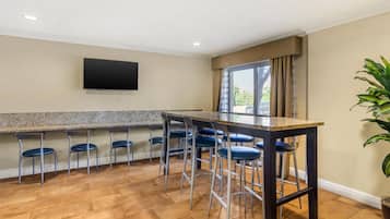 A kitchen with a granite countertop, bar stools, and a flat-screen TV mounted on the wall.