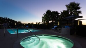 A heated outdoor swimming pool with lounge chairs and palm trees, surrounded by a fence and a building with illuminated signs. - The Marina Inn on San Francisco Bay (San Leandro)