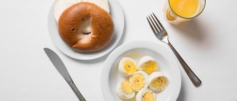 A breakfast plate with a bagel, boiled eggs, and a glass of orange juice on a white table.