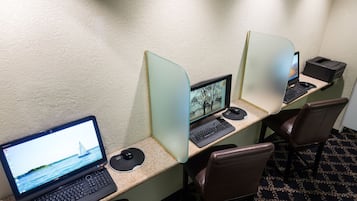Habitación de hotel con tres espacios de trabajo, cada uno equipado con una computadora, teclado y ratón. El piso es alfombrado y la pared es lisa.