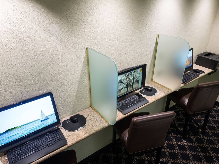 Habitación de hotel con tres espacios de trabajo, cada uno equipado con una computadora, teclado y ratón. El piso es alfombrado y la pared es lisa.