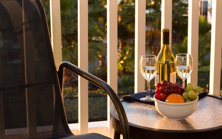 A dining table with a bowl of fruit, a bottle of wine, and two wine glasses.