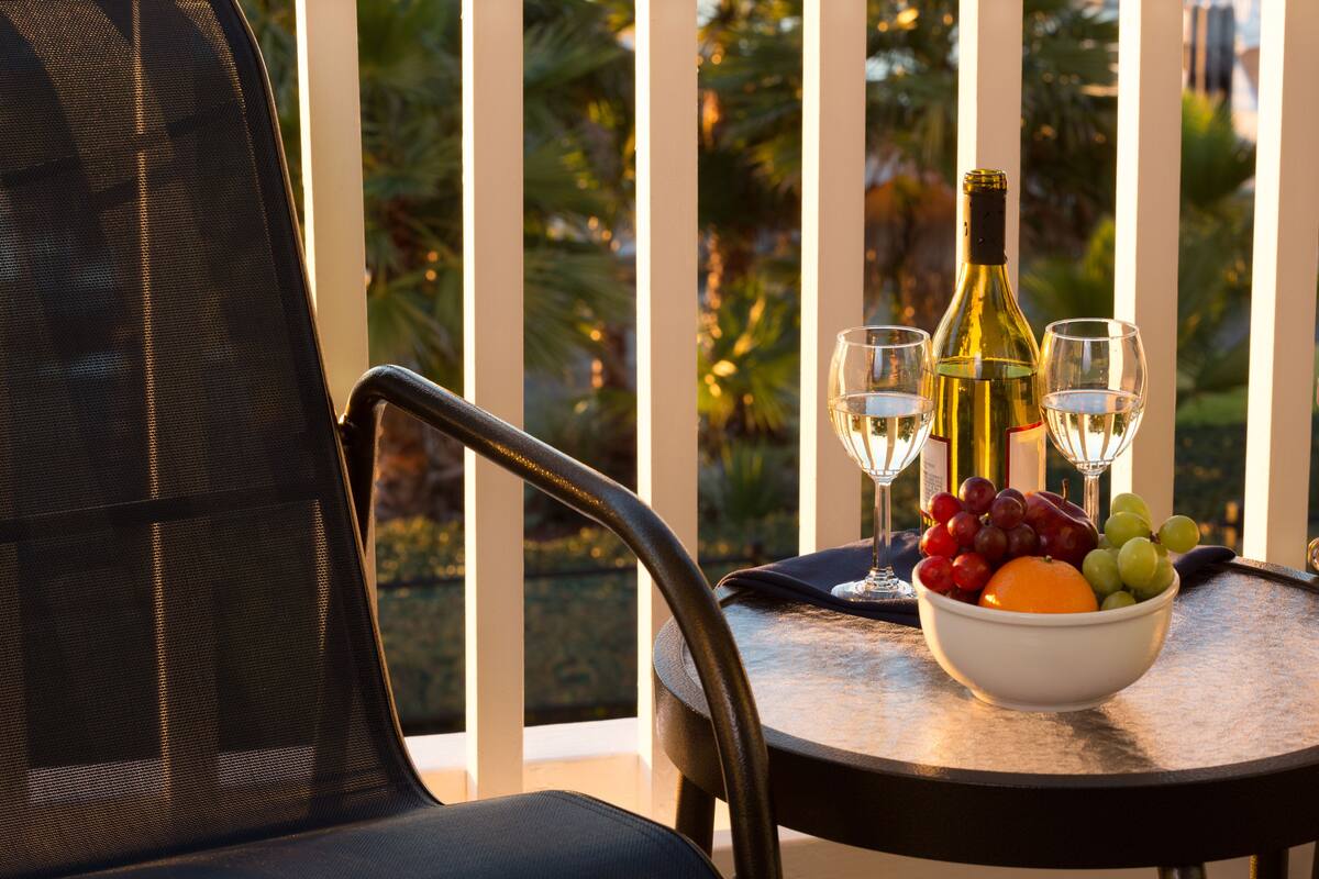 A dining table with a bowl of fruit, a bottle of wine, and two wine glasses.