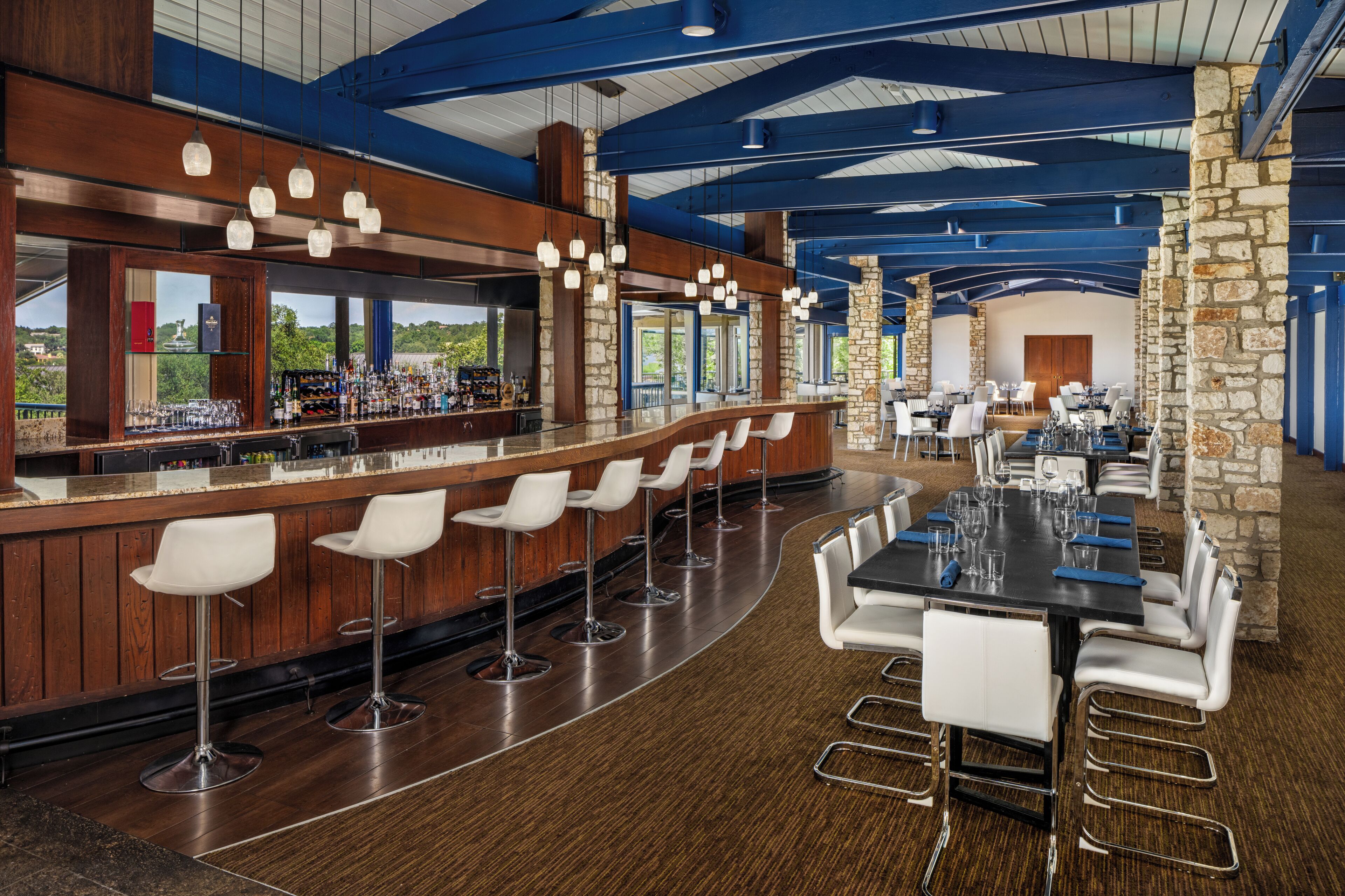 A bar area with a long counter, white bar stools, and a stone pillar.