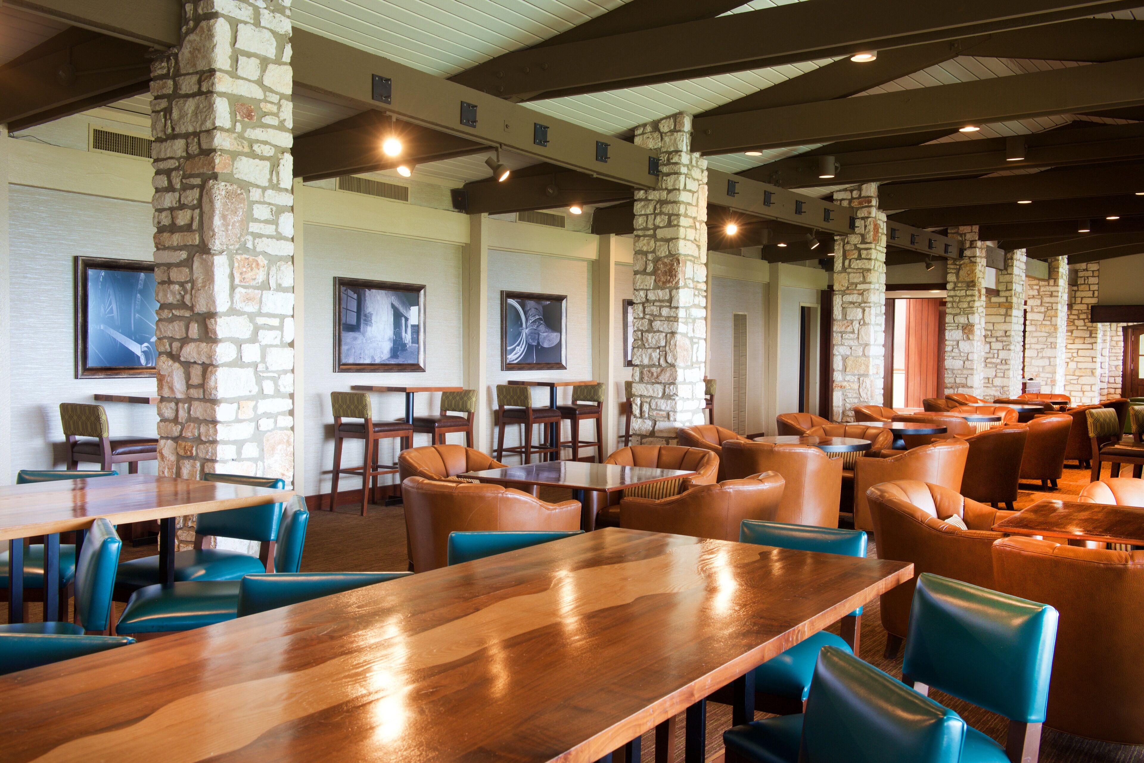 Een ruime restaurantzaal met stenen zuilen, houten tafels en lederen stoelen.