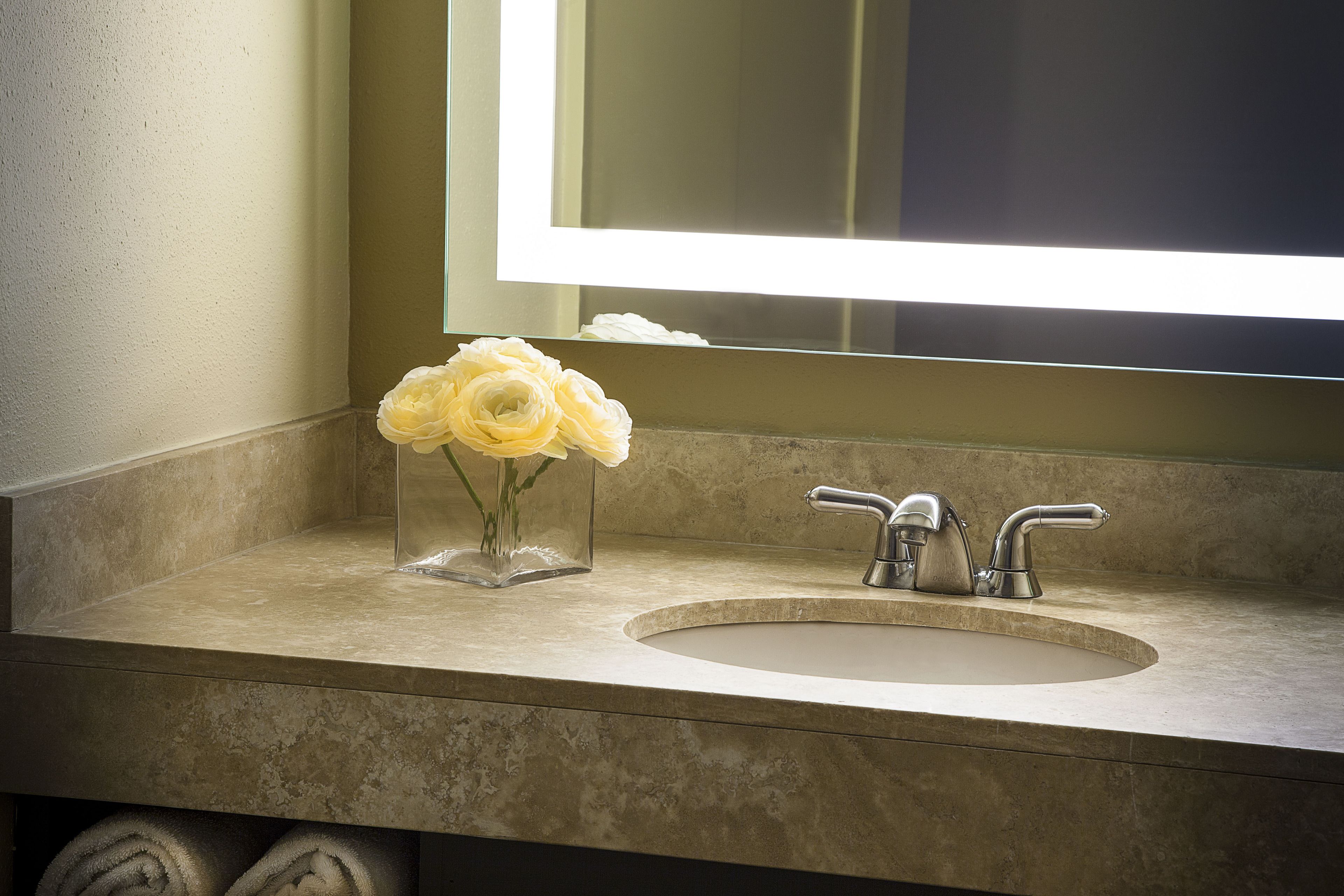 A bathroom with a sink, mirror, and a vase with flowers.