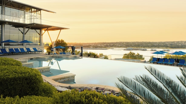 A modern hotel pool area with clear views of a body of water and a distant cityscape.