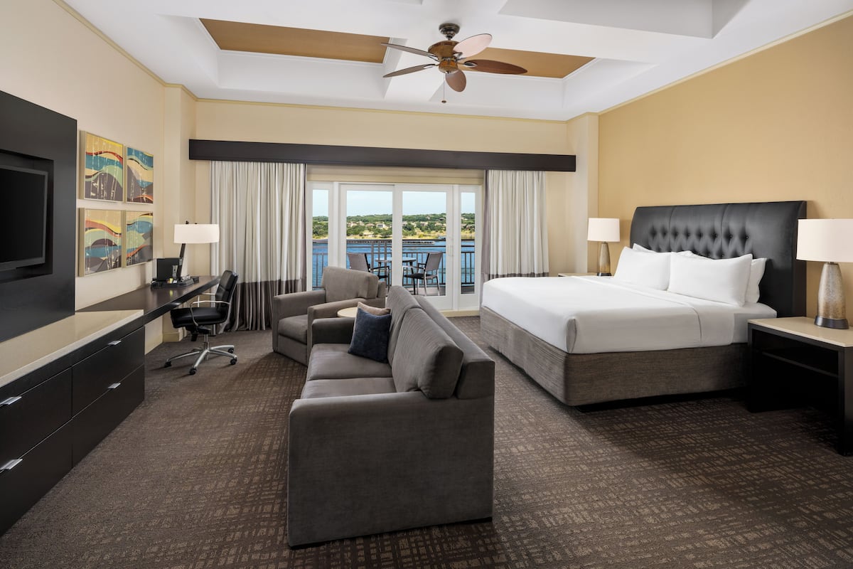 A hotel room with a bed, a sofa, a desk, a TV, and a balcony with a view.