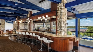 A bar area with a stone column, wooden bar counter, and white bar stools.