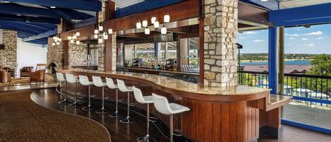 A bar area with a stone column, wooden bar counter, and white bar stools.