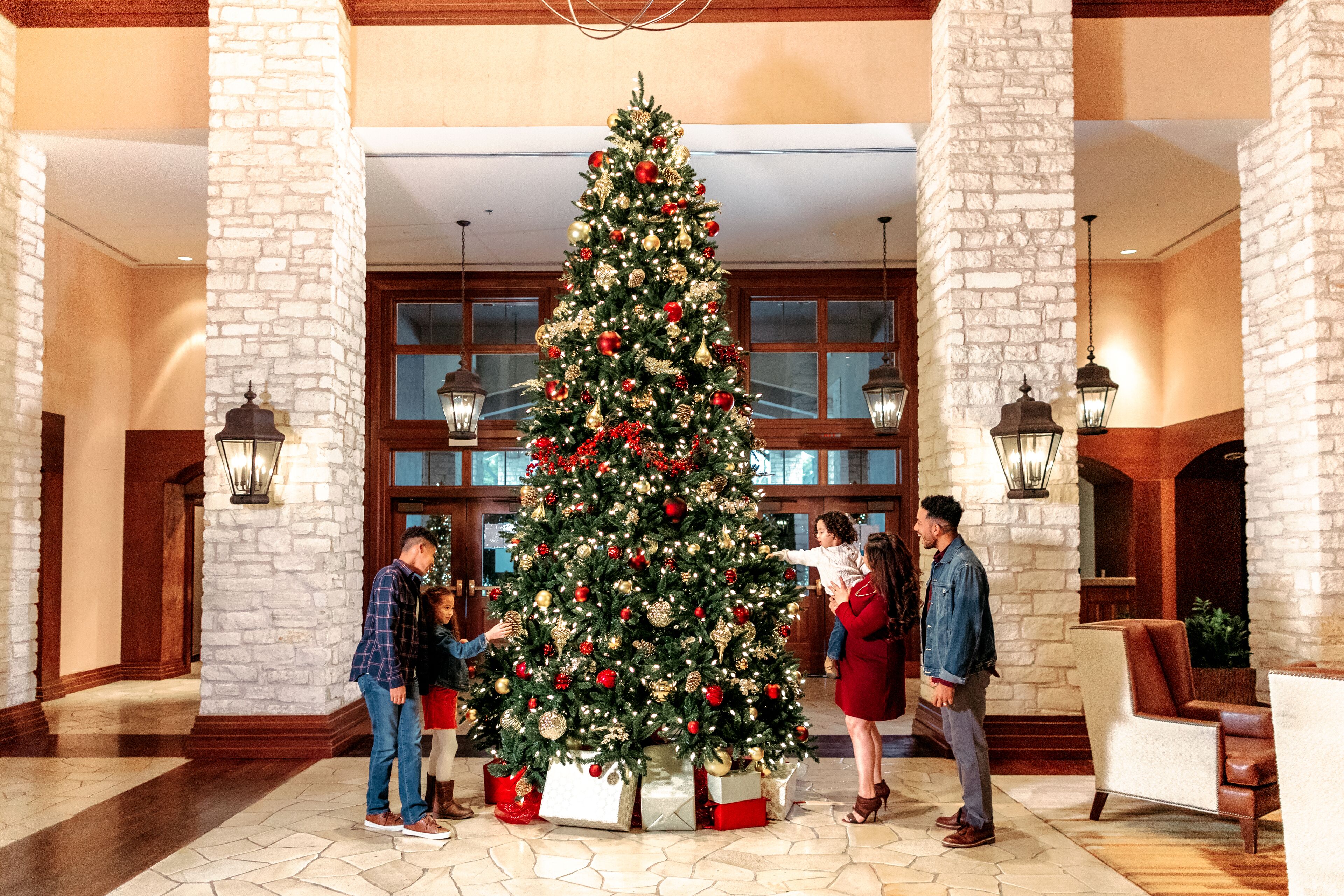 A lobby with a large Christmas tree, stone pillars, and a grand staircase.