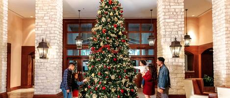 A lobby with a large Christmas tree, stone pillars, and a grand staircase.