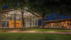 A modern building with large glass windows and a metal framework, surrounded by well-maintained grass and trees.