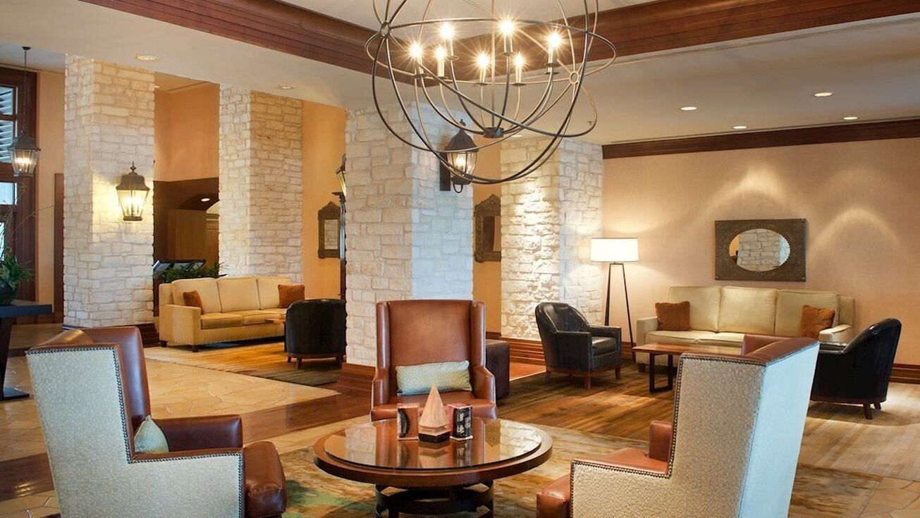 A lobby with a stone wall, leather armchairs, a round table, and a chandelier.