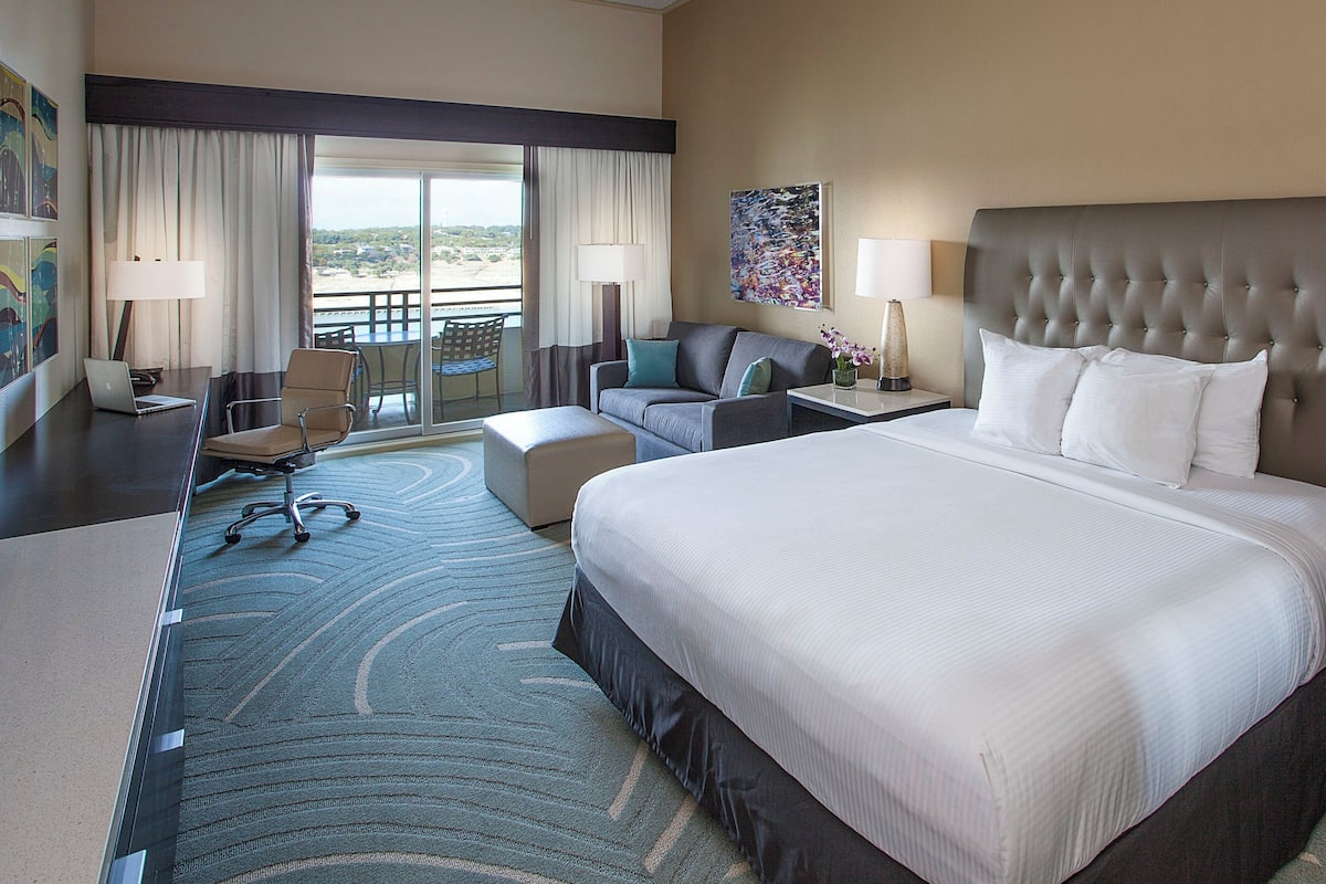 A hotel room with a large bed, a sofa, a desk with a laptop, a chair, and a view of the outdoors.