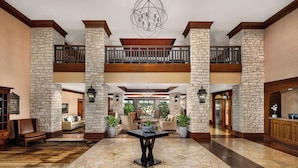 A spacious lobby with a stone floor, a central table, and a balcony overlooking the interior.