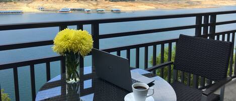 A balcony with a laptop, a cup of coffee, and a vase of yellow flowers.