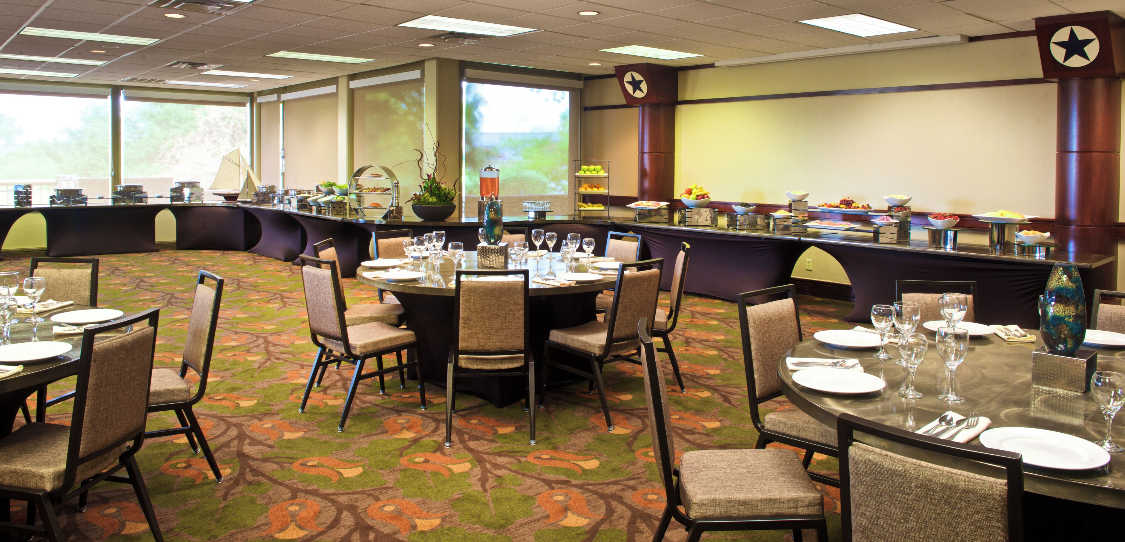 Een restaurantgedeelte in een hotel met ronde tafels gedekt voor maaltijden, stoelen en een buffet met diverse gerechten.