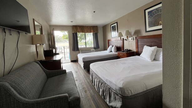 A hotel room with two beds, a sofa, a TV, and a window with curtains. - Fresno Inn (Fresno)