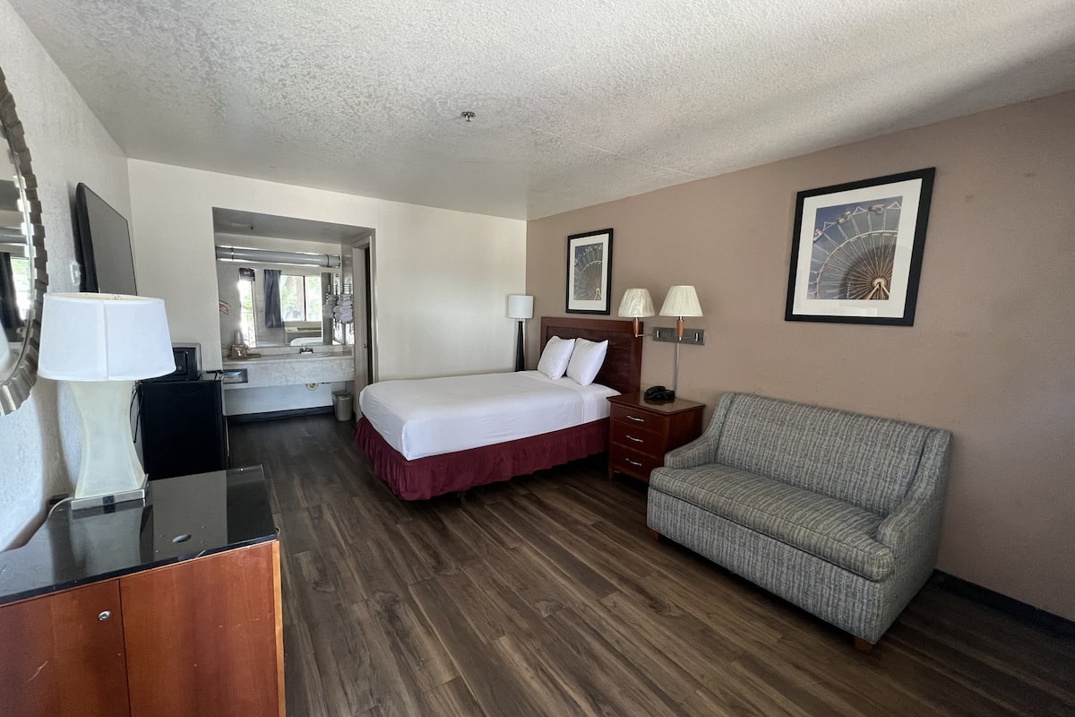A hotel room with a bed, a desk, a chair, and a bathroom visible through an open door.