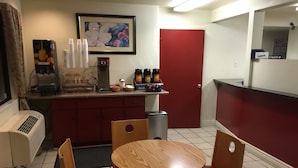 A small, compact room with a round wooden table and four chairs, a red door, a coffee machine, and a refrigerator. - Fresno Inn (Fresno)