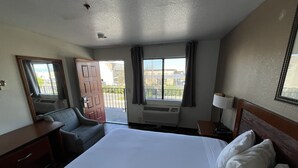 A hotel room with a large bed, a desk, a chair, a window with curtains, and a balcony. - Fresno Inn (Fresno)