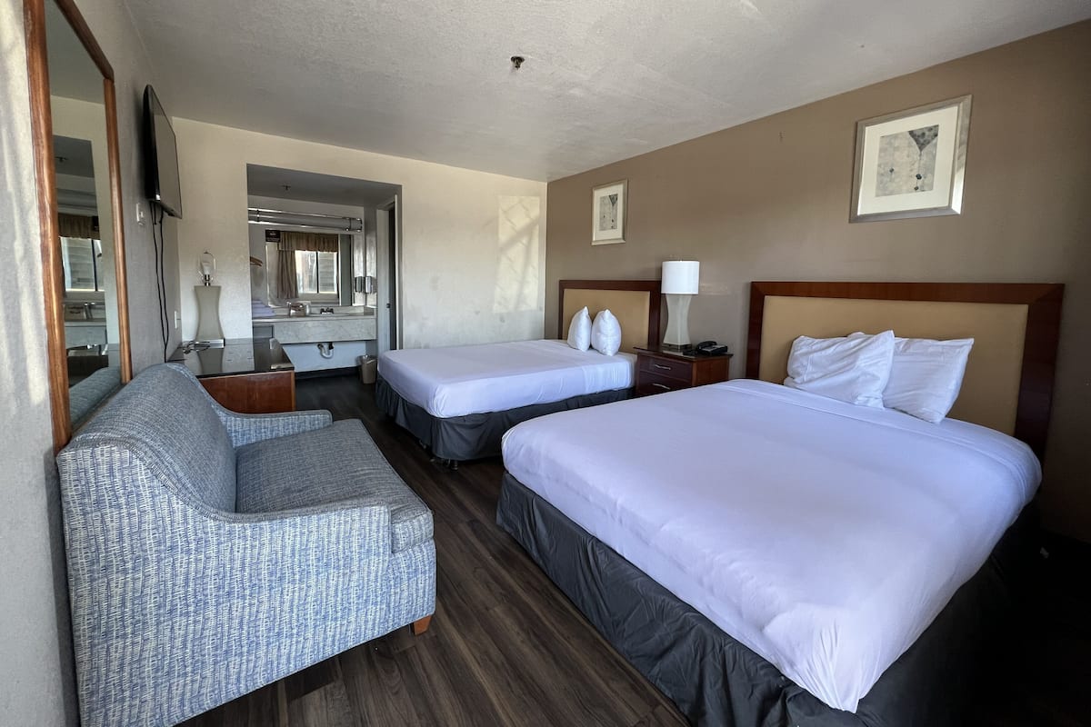 A hotel room with two beds, a sofa, a desk, a mirror, and a bathroom visible through an open door.