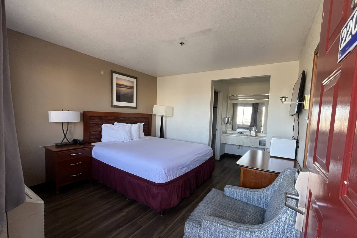 A hotel room with a bed, bedside tables, a desk, a chair, a mirror, and a door with a number plate.