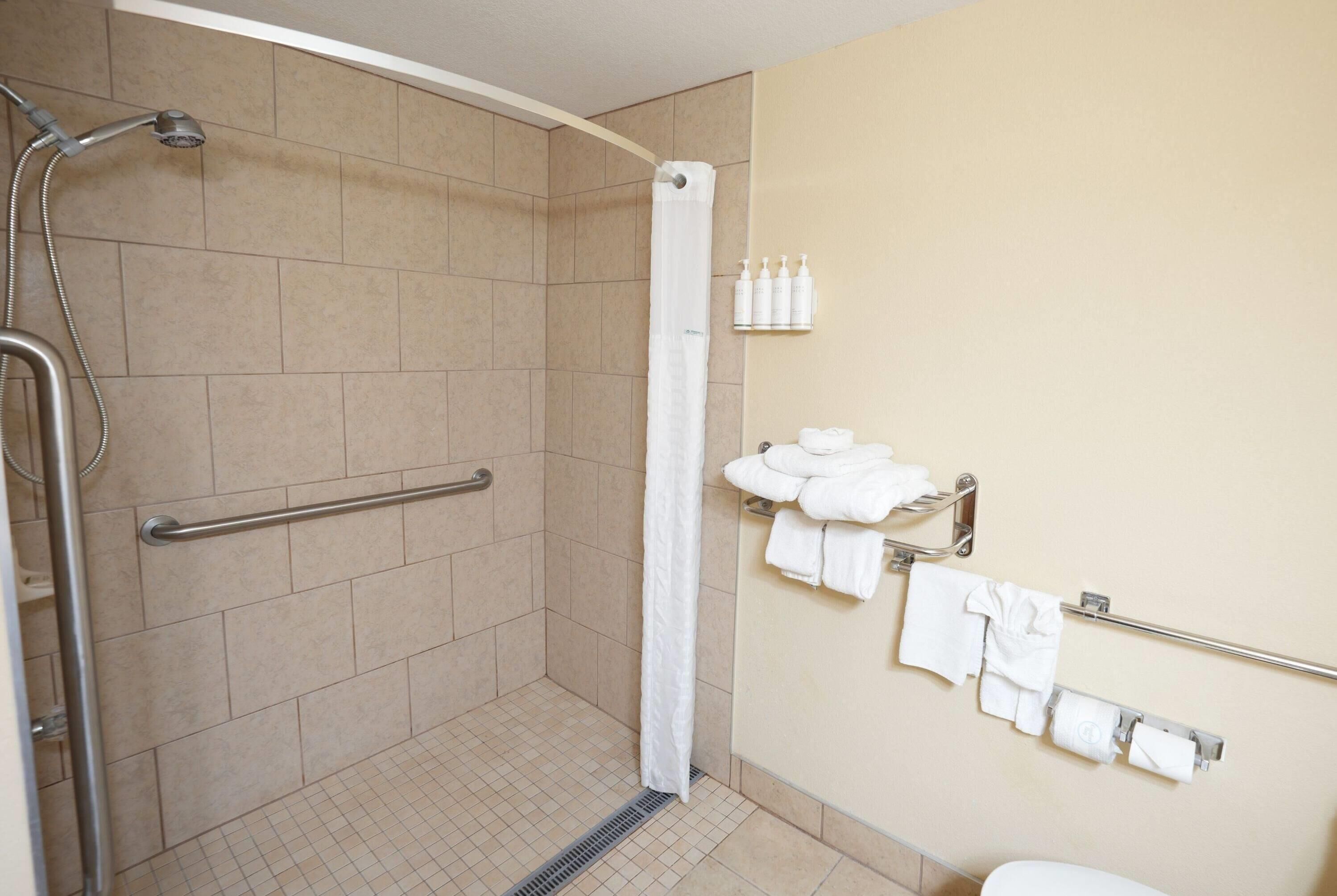 A shower area with a handrail, a white shower curtain, and a towel rack with towels.
