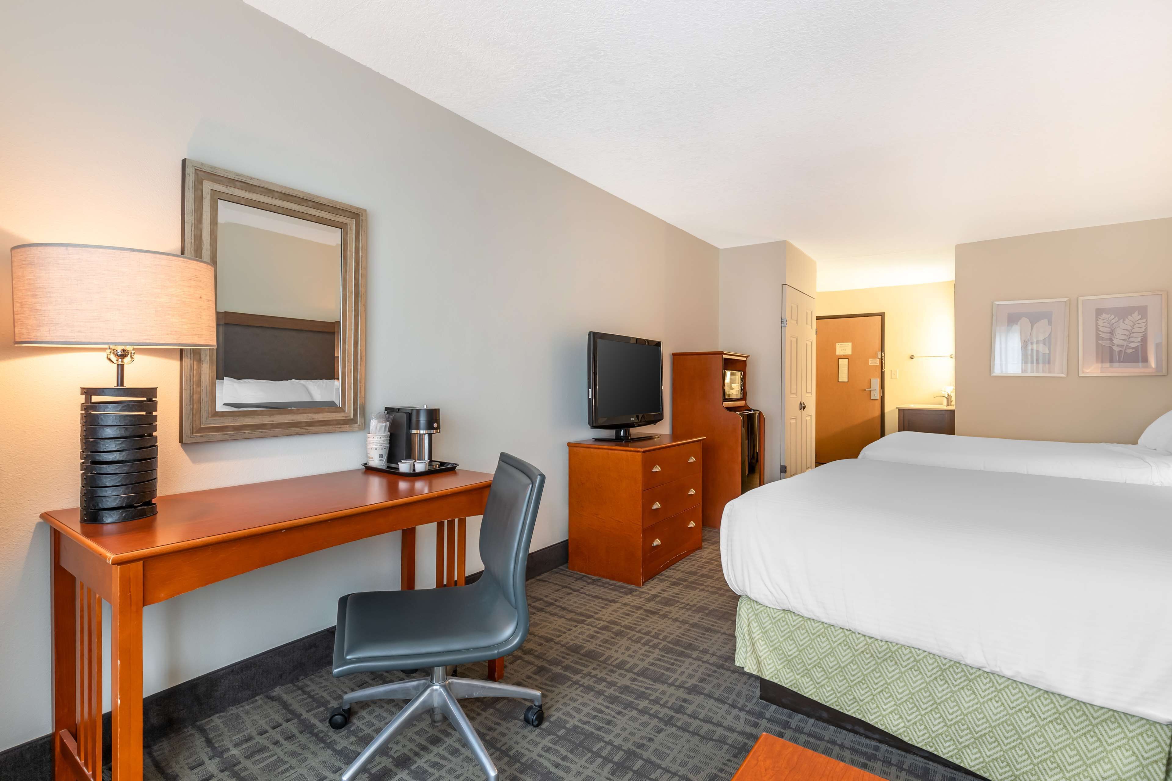 Ein Hotelzimmer mit Bett, Schreibtisch, Stuhl, Fernseher, Kommode und Spiegel.