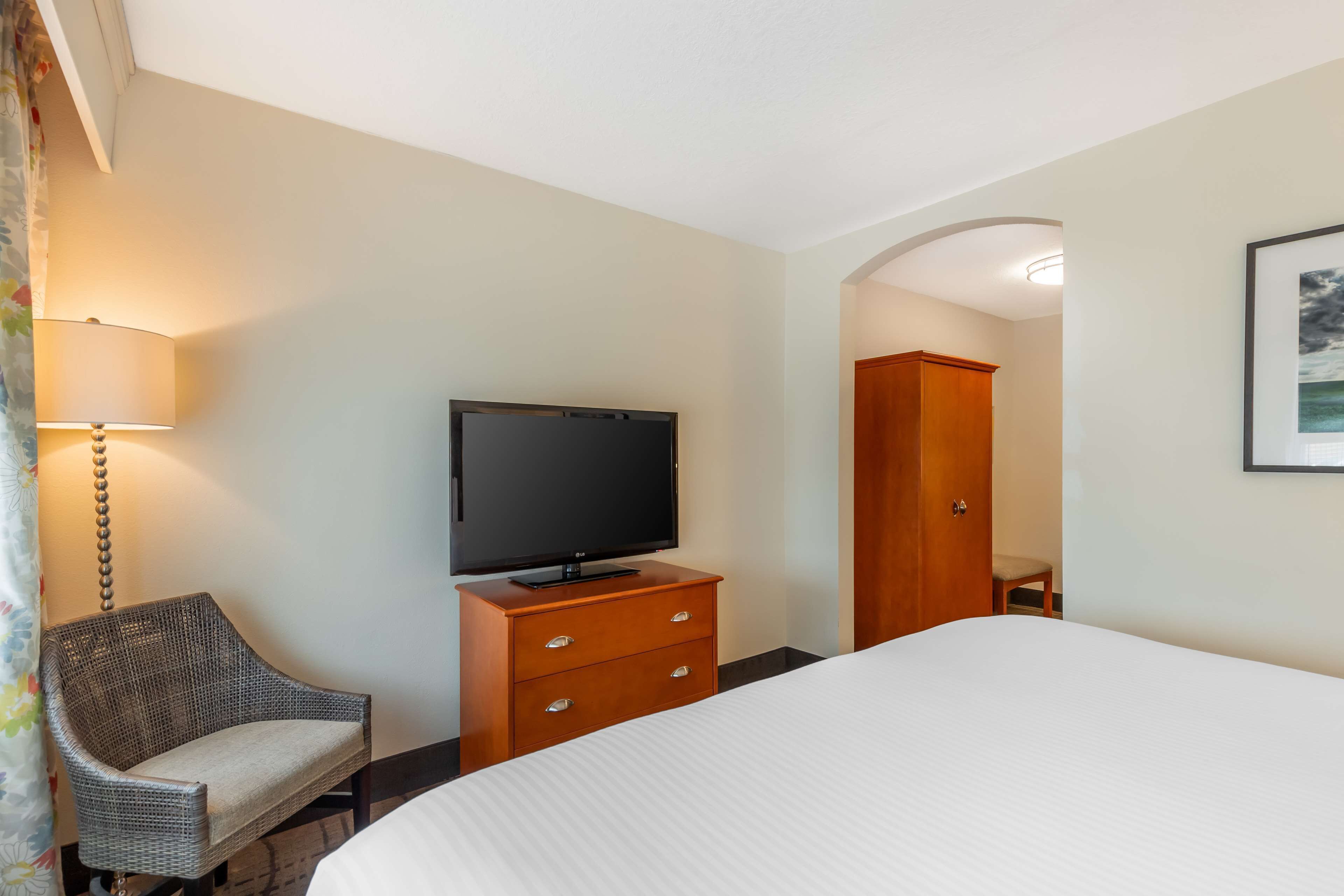 Ein Hotelzimmer mit einem Bett, einem Fernseher auf einer Holzkommode, einem Korbstuhl und einem Kleiderschrank.