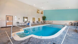 An indoor swimming pool with a blue water feature, a tiled floor, and a seating area with chairs and a plant.