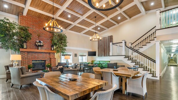 A spacious living area with a wooden dining table, comfortable seating, a brick fireplace, and a staircase leading to an upper level.