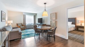 A hotel room with a dining area, a sofa, a TV, and a bed.