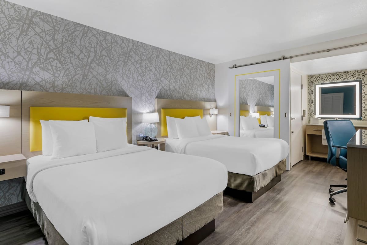 A hotel room with two beds, a desk, a chair, and a mirror.
