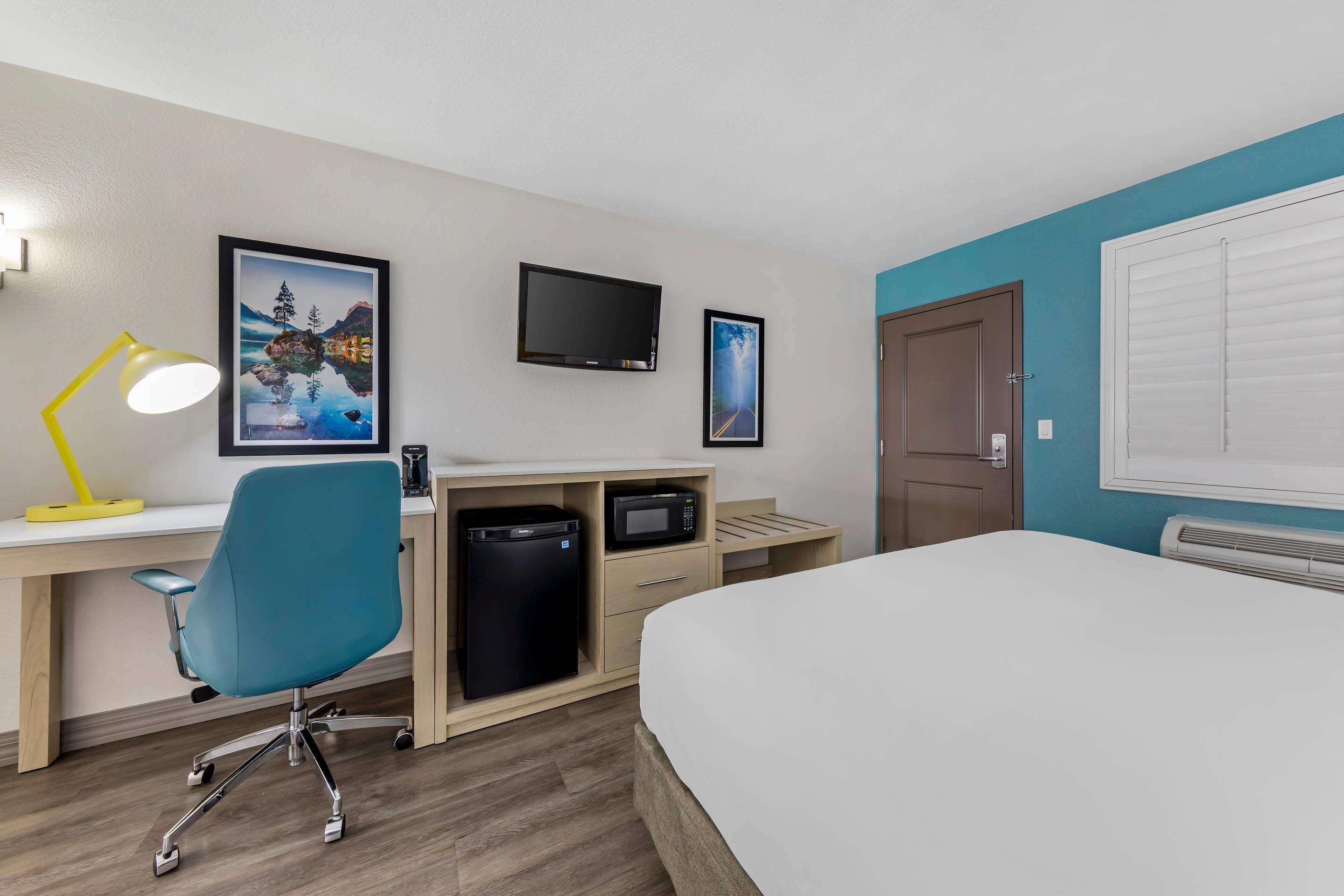 Een hotelkamer met een bed, bureau, stoel, televisie en een magnetron.