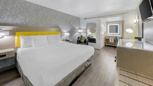 A hotel room with a large bed, bedside tables, a desk with a mirror, and a TV. - Hillstone Inn Tulare, an Ascend Collection Hotel (Tulare)