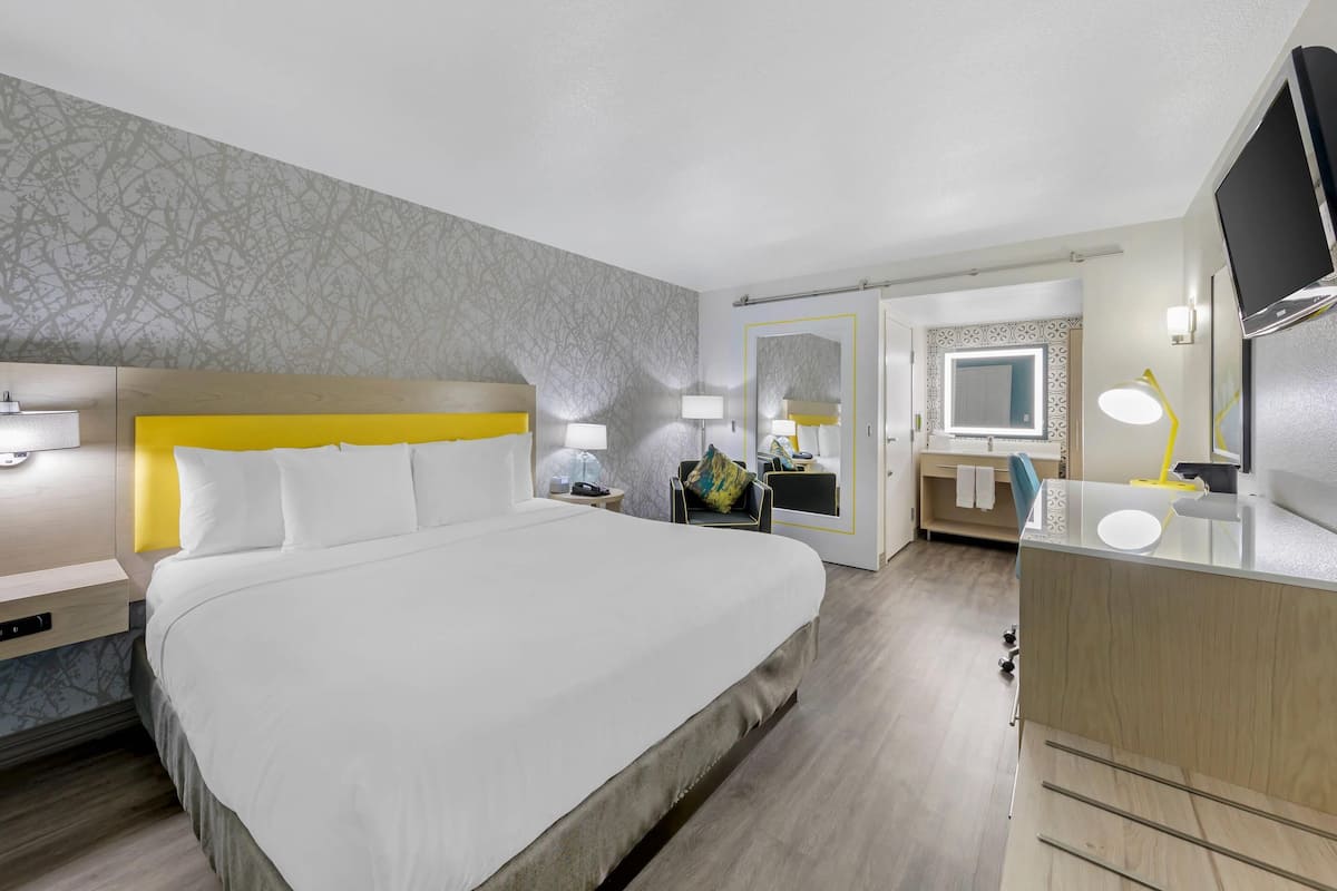 A hotel room with a large bed, bedside tables, a desk with a mirror, and a TV.