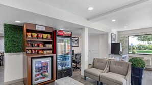 A modern lounge area with seating, a snack vending machine, a Coca-Cola refrigerator, and a view of the outdoors. - Hillstone Inn Tulare, an Ascend Collection Hotel (Tulare)
