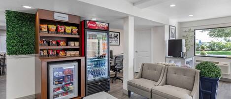 Et moderne loungeområde med møbler, en automat til snacks, et Coca-Cola køleskab og udsigt til det fri.