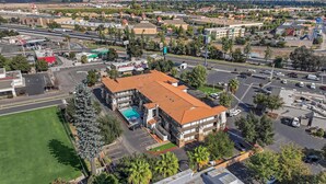 An aerial view of a multi-story hotel with a red-tiled roof, surrounded by parking areas and greenery. - Hillstone Inn Tulare, an Ascend Collection Hotel (Tulare)