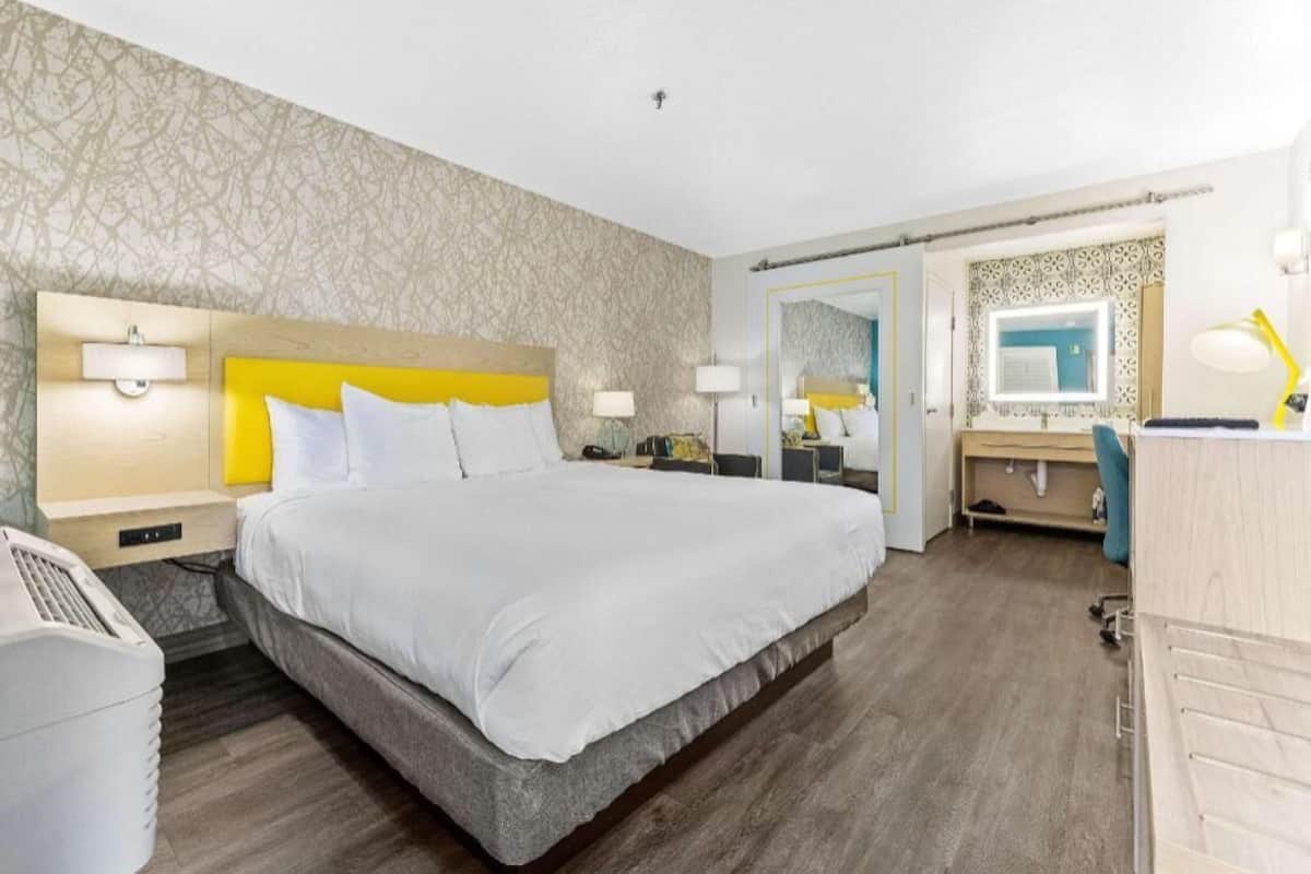 A hotel room with a large bed, bedside tables, a desk, a mirror, and a wardrobe.