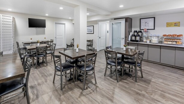 A modern dining area with wooden tables and chairs, a coffee station, and a flat-screen TV mounted on the wall. - Hillstone Inn Tulare, an Ascend Collection Hotel (Tulare)