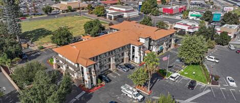 An aerial view of a commercial area with a multi-story building featuring a red-tiled roof, parking lots, and various businesses including a McDonald's and a Hillstone Inn.