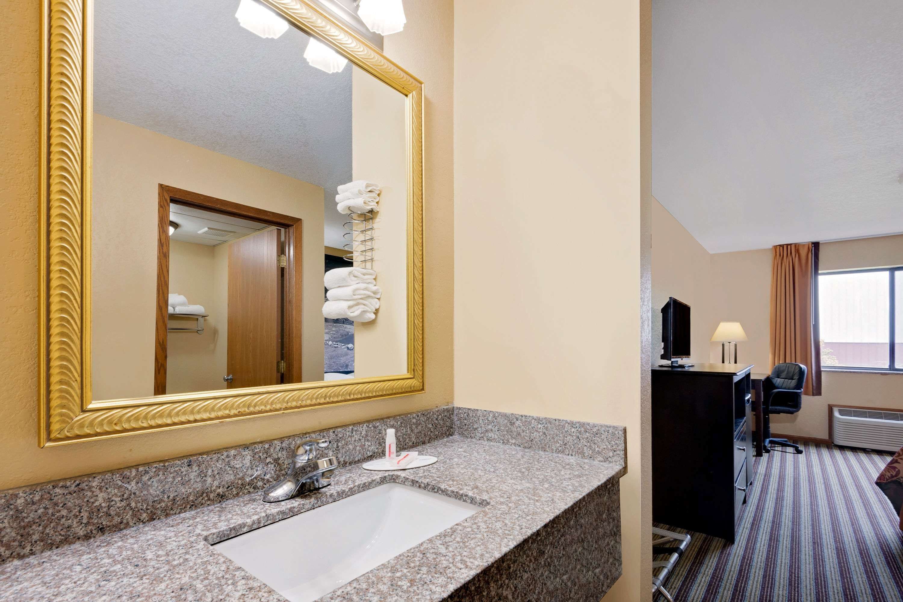 A hotel bathroom with a granite countertop sink, a large mirror, and a towel rack.