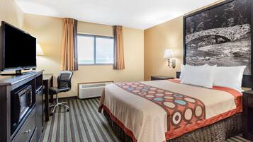 A hotel room with a bed, a TV, a desk, a chair, a window with curtains, a wall-mounted lamp, and a framed picture on the wall.