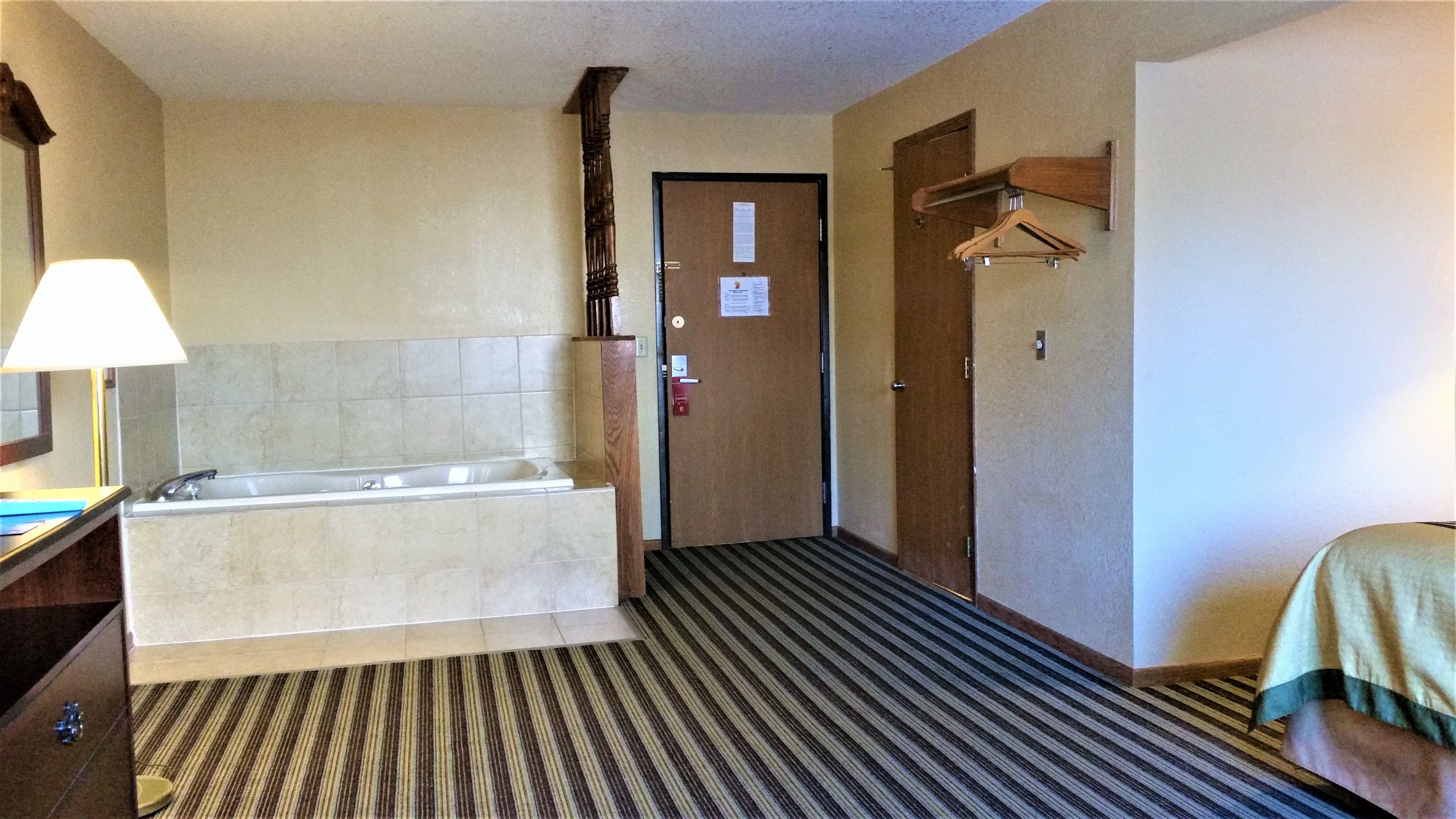 Un baño de hotel con una bañera, un lavamanos y un espejo. Hay una puerta con un letrero y un perchero.