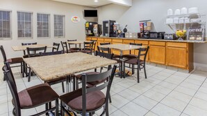 A restaurant with multiple tables and chairs, a kitchen area with appliances, and a counter with dishes and condiments. - Super 8 by Wyndham Iowa Falls (Iowa Falls)
