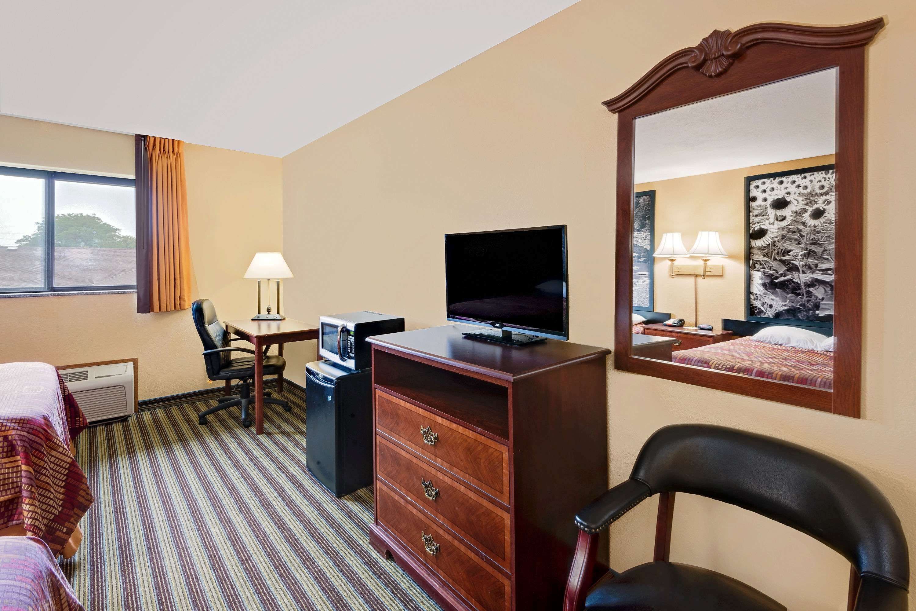 A hotel room with a bed, a desk with a computer, a TV, a dresser, a chair, and a large mirror.