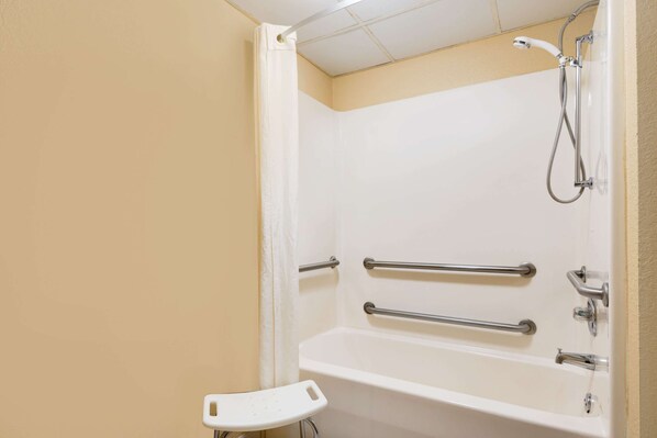 A bathroom with a white bathtub, grab bars, a showerhead, and a white shower seat. - Super 8 by Wyndham Iowa Falls (Iowa Falls)